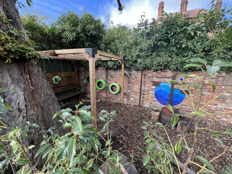 Backyard scene with a brick wall, green tire swings on a wooden frame, ivy over the wall, and a large tree trunk on the left.